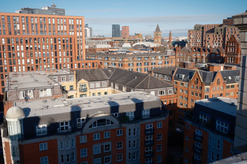 A city skyline featuring modern high-rise office buildings and historic brick structures in London, with a clear blue sky above. The scene includes glass-clad towers reflecting sunlight and traditiona